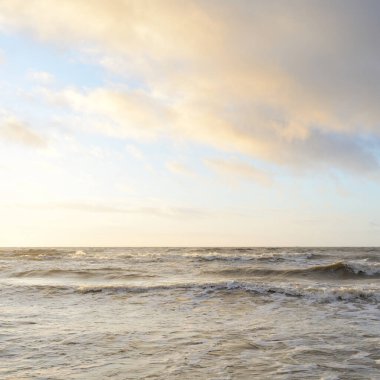 Gün batımında Baltık Denizi. Dramatik gökyüzü, mavi ve pembe parlayan bulutlar, altın güneş ışığı. Dalgalar, su sıçratma. Resimli manzara, deniz manzarası, doğa. Panoramik görünüm,