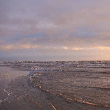 Fırtınadan sonra gün batımında Baltık Denizi. Dramatik gökyüzü, parlayan bulutlar, dofty altın güneş ışığı, dalgalar, fışkıran su. Resimli panoramik manzara. Doğa, çevre, ekoloji