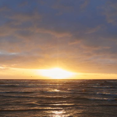Fırtınadan sonra gün batımında Baltık Denizi. Dramatik gökyüzü, parlayan bulutlar, dofty altın güneş ışığı, dalgalar, fışkıran su. Resimli panoramik manzara. Doğa, çevre, ekoloji
