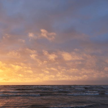 Fırtınadan sonra gün batımında Baltık Denizi. Dramatik gökyüzü, parlayan bulutlar, dofty altın güneş ışığı, dalgalar, fışkıran su. Resimli panoramik manzara. Doğa, çevre, ekoloji