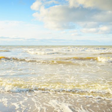 Kumlu bir sahilden (kum tepeleri) Baltık denizinin panoramik görüntüsü. Parlayan bulutlarla, dalgalarla ve su sıçramalarıyla berrak bir gökyüzü. Idyllic deniz manzarası. Sıcak kış havası, iklim değişikliği, doğa