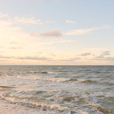 Gün batımında Baltık kıyıları (kum tepeleri). Yumuşak güneş ışığı, parlayan bulutlar, dalgalar ve su fışkıran berrak gökyüzü. Idyllic deniz manzarası. Liepaja, Letonya, Avrupa. Sıcak kış havası, iklim değişikliği, doğa