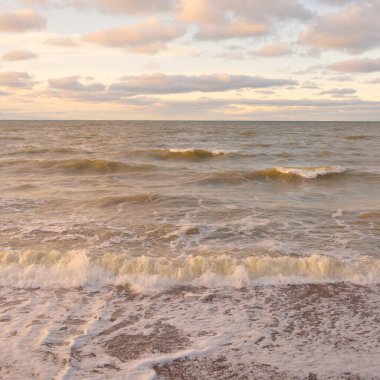 Gün batımında Baltık kıyıları (kum tepeleri). Yumuşak güneş ışığı, parlayan bulutlar, dalgalar ve su fışkıran berrak gökyüzü. Idyllic deniz manzarası. Liepaja, Letonya, Avrupa. Sıcak kış havası, iklim değişikliği, doğa