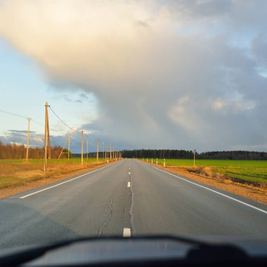 Gün batımında tarla ve orman boyunca asfalt yol (karayolu). Arabadan görüntü. Turizm, tatiller, uzak yerler, lojistik kavramlar