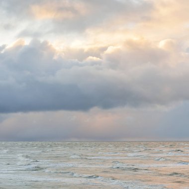 Fırtınadan sonra Baltık Denizi. Dramatik gökyüzü, parlayan bulutlar, yumuşak güneş ışığı. Dalgalar, su sıçratma. Resimli manzara, deniz manzarası, doğa. Panoramik görünüm