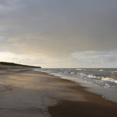 Gün batımında Baltık kıyıları (kum tepeleri). Yumuşak güneş ışığı, parlayan bulutlar, dalgalar ve su fışkıran berrak gökyüzü. Idyllic deniz manzarası. Liepaja, Letonya, Avrupa. Sıcak kış havası, iklim değişikliği, doğa