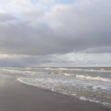 Kumlu bir sahilden (kum tepeleri) Baltık denizinin panoramik görüntüsü. Koyu bulutlu dramatik bir gökyüzü. Dalgalar, su sıçramaları. Idyllic deniz manzarası. Sıcak kış havası, iklim değişikliği, doğa. Danimarka