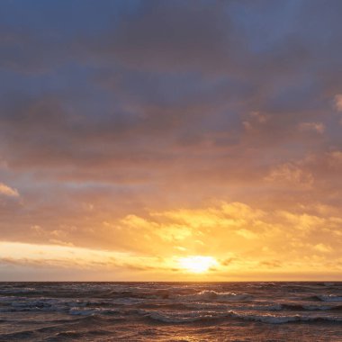 Fırtınadan sonra gün batımında Baltık Denizi. Dramatik gökyüzü, parlayan bulutlar, dofty altın güneş ışığı, dalgalar, fışkıran su. Resimli panoramik manzara. Doğa, çevre, ekoloji