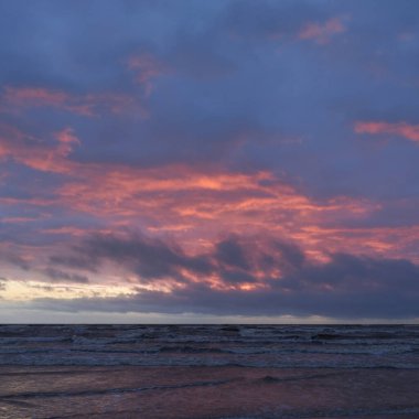 Fırtınadan sonra gün batımında Baltık Denizi. Dramatik gökyüzü, parlayan bulutlar, dofty altın güneş ışığı, dalgalar, fışkıran su. Resimli panoramik manzara. Doğa, çevre, ekoloji