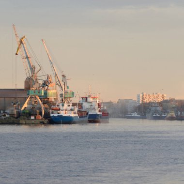 Gemi ve balıkçı teknesi bir ticaret limanına demir attı. Vinçler arka planda. Liepaja, Letonya, Baltık Denizi. Nakliye, lojistik, küresel iletişim, endüstri, ekonomi