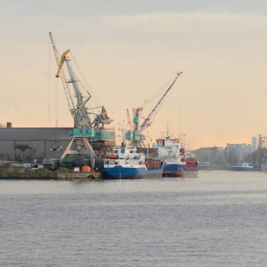 Ship and fishing boat anchored in a trading port. Cranes in the background. Liepaja, Latvia, Baltic sea. Freight transportation, logistics, global communications, industry, economy