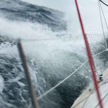 Açık denizde yelken açan topuklu bir yat. Güverte ve donanım görüntüsü. Karanlık fırtına dalgaları, su sıçramaları. Uzun pozlama, hareket. Kötü hava, kasırga, tehlike. Yarış, yarış, spor