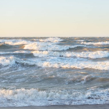 Gün batımında Baltık kıyısı. Yumuşak altın güneş ışığı, parlayan gökyüzü, dalgalar. Idyllic deniz manzarası. Seyahat yerleri, eko turizm, doğa, hava durumu, iklim değişikliği. Resimli panoramik manzara