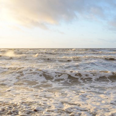 Gün batımında Baltık Denizi. Dramatik gökyüzü, mavi ve pembe parlayan bulutlar, altın güneş ışığı. Dalgalar, su sıçratma. Resimli manzara, deniz manzarası, doğa. Panoramik görünüm,