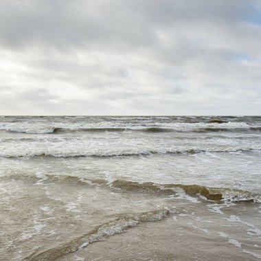 Kumlu sahilden Baltık denizinin panoramik görüntüsü (kum tepeleri). Parlak bulutlu dramatik bir gökyüzü. Dalgalar, su sıçramaları. Idyllic deniz manzarası. Bahar havası, iklim değişikliği, doğa