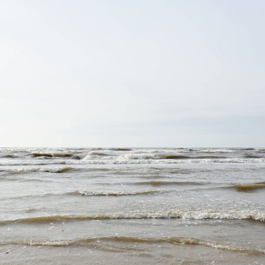 Gün batımında Baltık kıyısı. Yumuşak güneş ışığı, parlayan bulutlar, dalgalar ve su fışkıran berrak gökyüzü. Idyllic deniz manzarası. Hava, iklim değişikliği, doğa
