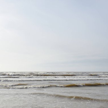 Gün batımında Baltık kıyısı. Yumuşak güneş ışığı, parlayan bulutlar, dalgalar ve su fışkıran berrak gökyüzü. Idyllic deniz manzarası. Hava, iklim değişikliği, doğa