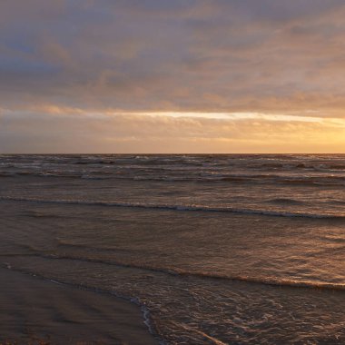 Fırtınadan sonra gün batımında Baltık Denizi. Dramatik gökyüzü, parlayan bulutlar, dofty altın güneş ışığı, dalgalar, fışkıran su. Resimli panoramik manzara. Doğa, çevre, ekoloji