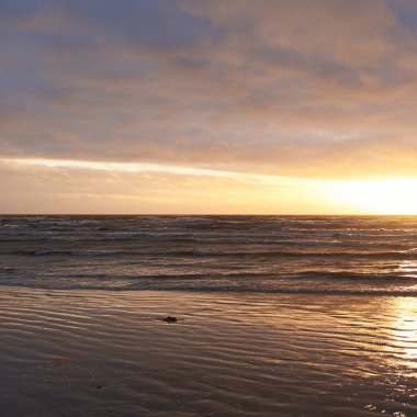 Fırtınadan sonra gün batımında Baltık Denizi. Dramatik gökyüzü, parlayan bulutlar, dofty altın güneş ışığı, dalgalar, fışkıran su. Resimli panoramik manzara. Doğa, çevre, ekoloji