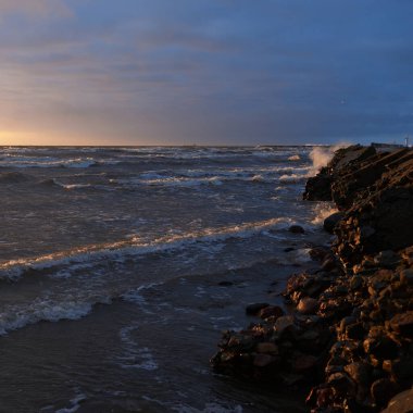 Fırtınadan sonra gün batımında Baltık Denizi. Dramatik gökyüzü, parlayan bulutlar, dofty altın güneş ışığı, dalgalar, fışkıran su. Resimli panoramik manzara. Doğa, çevre, ekoloji
