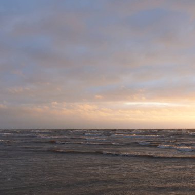 Fırtınadan sonra gün batımında Baltık Denizi. Dramatik gökyüzü, parlayan bulutlar, dofty altın güneş ışığı, dalgalar, fışkıran su. Resimli panoramik manzara. Doğa, çevre, ekoloji