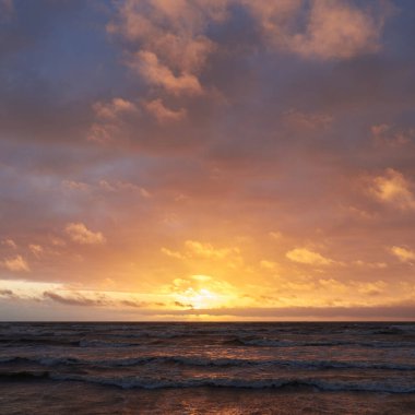 Fırtınadan sonra gün batımında Baltık Denizi. Dramatik gökyüzü, parlayan bulutlar, dofty altın güneş ışığı, dalgalar, fışkıran su. Resimli panoramik manzara. Doğa, çevre, ekoloji