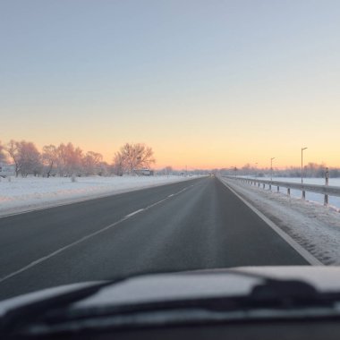 Karla kaplı orman ve kırsal alanda boş otoyol (asfalt yol). Gündoğumu, kar yağışı. Avrupa. Doğa, Noel tatilleri, uzak yerler, kış lastikleri, tehlikeli sürüş konsepti