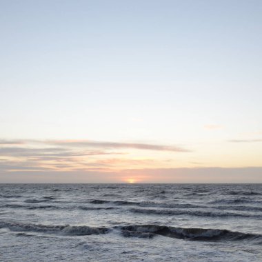 Gün batımında Baltık Denizi. Dramatik gökyüzü, mavi ve pembe parlayan bulutlar, altın güneş ışığı. Dalgalar, su sıçratma. Resimli manzara, deniz manzarası, doğa. Panoramik görünüm,