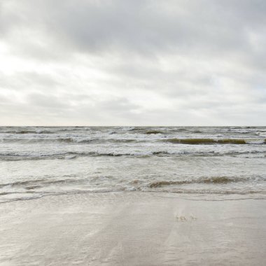 Kumlu sahilden Baltık denizinin panoramik görüntüsü (kum tepeleri). Parlak bulutlu dramatik bir gökyüzü. Dalgalar, su sıçramaları. Idyllic deniz manzarası. Bahar havası, iklim değişikliği, doğa