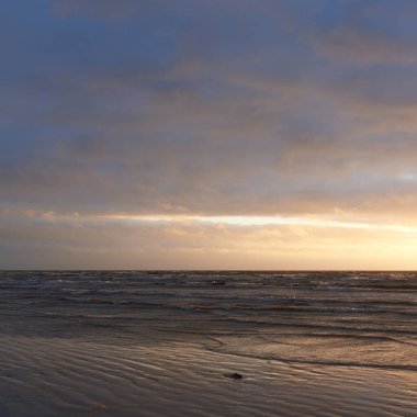 Fırtınadan sonra gün batımında Baltık Denizi. Dramatik gökyüzü, parlayan bulutlar, dofty altın güneş ışığı, dalgalar, fışkıran su. Resimli panoramik manzara. Doğa, çevre, ekoloji