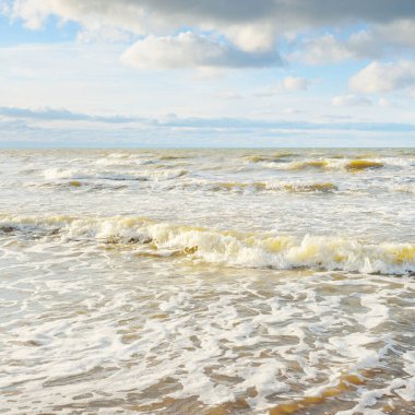 Kumlu bir sahilden (kum tepeleri) Baltık denizinin panoramik görüntüsü. Parlayan bulutlarla, dalgalarla ve su sıçramalarıyla berrak bir gökyüzü. Idyllic deniz manzarası. Sıcak kış havası, iklim değişikliği, doğa