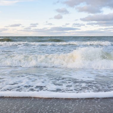 Gün batımında Baltık kıyıları (kum tepeleri). Yumuşak güneş ışığı, parlayan bulutlar, dalgalar ve su fışkıran berrak gökyüzü. Idyllic deniz manzarası. Liepaja, Letonya, Avrupa. Sıcak kış havası, iklim değişikliği, doğa