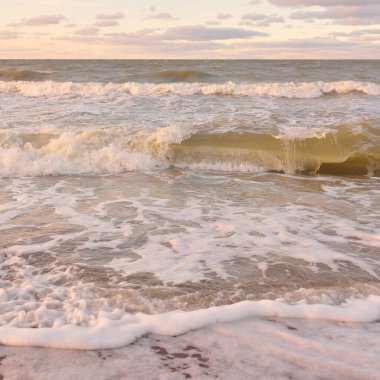 Gün batımında Baltık kıyıları (kum tepeleri). Yumuşak güneş ışığı, parlayan bulutlar, dalgalar ve su fışkıran berrak gökyüzü. Idyllic deniz manzarası. Liepaja, Letonya, Avrupa. Sıcak kış havası, iklim değişikliği, doğa