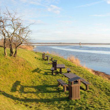 Modern dinlenme alanı, orman parkı, göl. Tahta banklar, masalar. Kamp alanı. Yumuşak güneş ışığı, açık gökyüzü. Baharın başında. Idyllic manzara. Doğa, çevre, ekoloji, eko-turizm, tatiller, hafta sonu