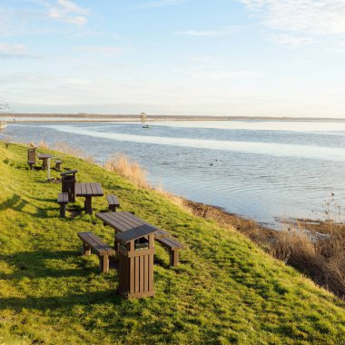 Modern dinlenme alanı, orman parkı, göl. Tahta banklar, masalar. Kamp alanı. Yumuşak güneş ışığı, açık gökyüzü. Baharın başında. Idyllic manzara. Doğa, çevre, ekoloji, eko-turizm, tatiller, hafta sonu