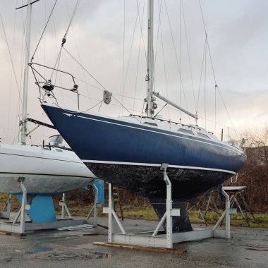 Mavi yelkenli donanımlı yelkenli bir yat kulübünde karada duruyor. Hizmet, onarım, ulaşım, spor, eğlence, eğlence aktivitesi