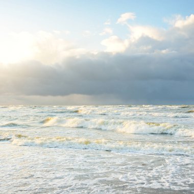 Fırtınadan sonra Baltık Denizi. Dramatik gökyüzü, parlayan bulutlar, yumuşak güneş ışığı. Dalgalar, su sıçratma. Resimli manzara, deniz manzarası, doğa. Panoramik görünüm