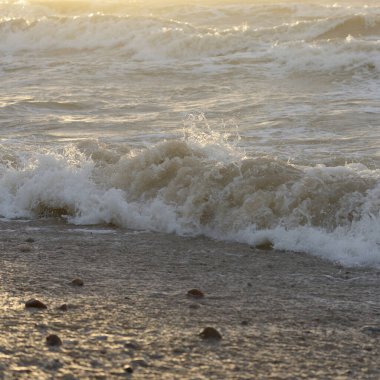 Fırtınadan sonra Baltık kıyıları. Gün batımı, yumuşak güneş ışığı. Su yüzeyi dokusu, çarpan dalgalar, sıçramalar, köpük. Resimli panoramik manzara. Idyllic deniz manzarası. Doğa, çevre, ekoloji temaları