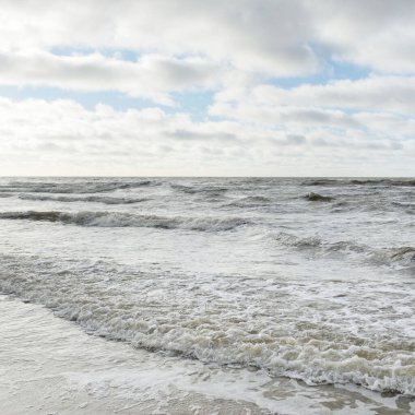 Fırtınadan sonra Baltık Denizi. Dramatik gökyüzü, parlayan bulutlar, yumuşak güneş ışığı. Dalgalar, su sıçratma. Resimli manzara, deniz manzarası, doğa. Panoramik görünüm