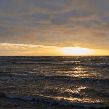 Fırtınadan sonra gün batımında Baltık Denizi. Dramatik gökyüzü, parlayan bulutlar, dofty altın güneş ışığı, dalgalar, fışkıran su. Resimli panoramik manzara. Doğa, çevre, ekoloji
