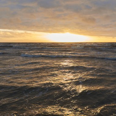 Fırtınadan sonra gün batımında Baltık Denizi. Dramatik gökyüzü, parlayan bulutlar, dofty altın güneş ışığı, dalgalar, fışkıran su. Resimli panoramik manzara. Doğa, çevre, ekoloji