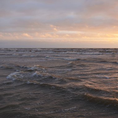 Fırtınadan sonra gün batımında Baltık Denizi. Dramatik gökyüzü, parlayan bulutlar, dofty altın güneş ışığı, dalgalar, fışkıran su. Resimli panoramik manzara. Doğa, çevre, ekoloji