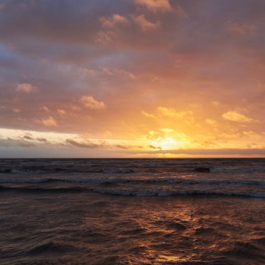 Fırtınadan sonra gün batımında Baltık Denizi. Dramatik gökyüzü, parlayan bulutlar, dofty altın güneş ışığı, dalgalar, fışkıran su. Resimli panoramik manzara. Doğa, çevre, ekoloji