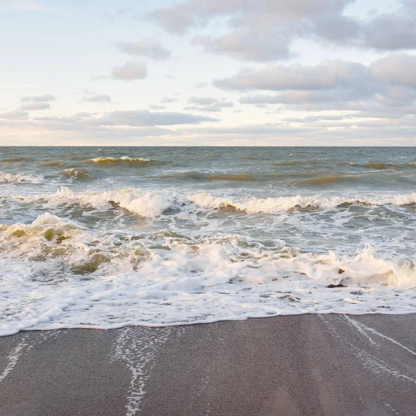 Gün batımında Baltık kıyıları (kum tepeleri). Yumuşak güneş ışığı, parlayan bulutlar, dalgalar ve su fışkıran berrak gökyüzü. Idyllic deniz manzarası. Liepaja, Letonya, Avrupa. Sıcak kış havası, iklim değişikliği, doğa