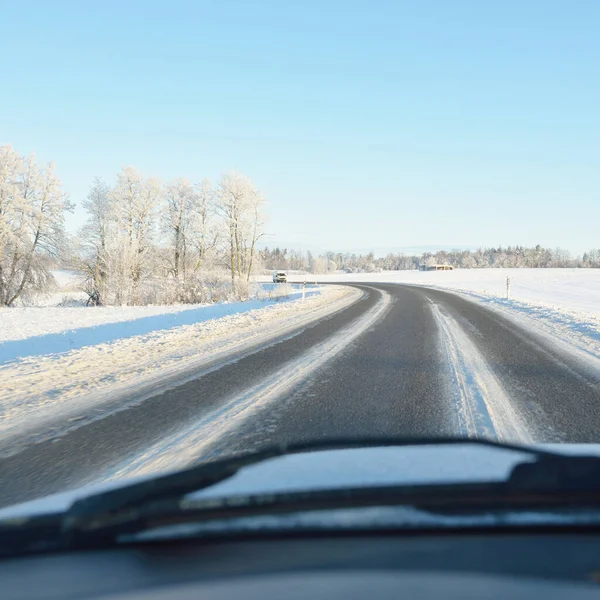 Empty highway (asphalt road) through the snow-covered forest and fields, rural area. Snow drifts. Europe. Nature, christmas vacations, remote places, winter tires, dangerous driving concept