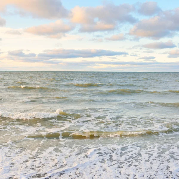 Gün batımında Baltık kıyıları (kum tepeleri). Yumuşak güneş ışığı, parlayan bulutlar, dalgalar ve su fışkıran berrak gökyüzü. Idyllic deniz manzarası. Liepaja, Letonya, Avrupa. Sıcak kış havası, iklim değişikliği, doğa