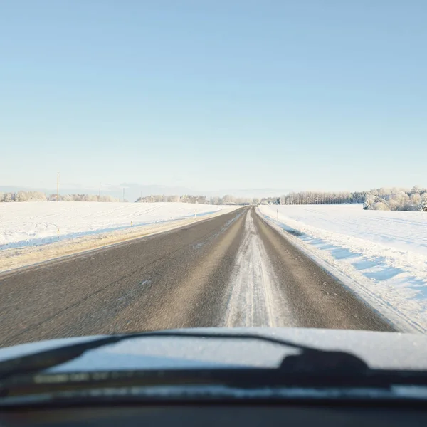 Empty highway (asphalt road) through the snow-covered forest and fields, rural area. Snow drifts. Europe. Nature, christmas vacations, remote places, winter tires, dangerous driving concept