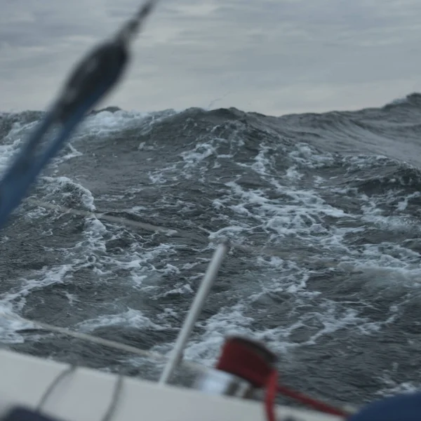 Açık denizde yelken açan topuklu bir yat. Kırmızı vinç ve donanım. Karanlık fırtına dalgaları, su sıçramaları. Uzun pozlama, hareket. Kötü hava, kasırga, tehlike. Yarış, yarış, spor