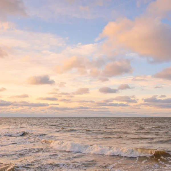 Gün batımında Baltık kıyıları (kum tepeleri). Yumuşak güneş ışığı, parlayan bulutlar, dalgalar ve su fışkıran berrak gökyüzü. Idyllic deniz manzarası. Liepaja, Letonya, Avrupa. Sıcak kış havası, iklim değişikliği, doğa