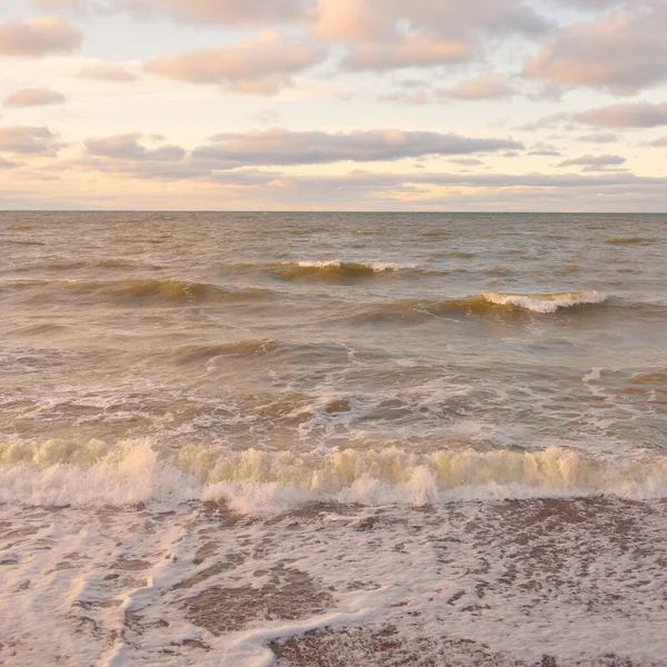 Gün batımında Baltık kıyıları (kum tepeleri). Yumuşak güneş ışığı, parlayan bulutlar, dalgalar ve su fışkıran berrak gökyüzü. Idyllic deniz manzarası. Liepaja, Letonya, Avrupa. Sıcak kış havası, iklim değişikliği, doğa